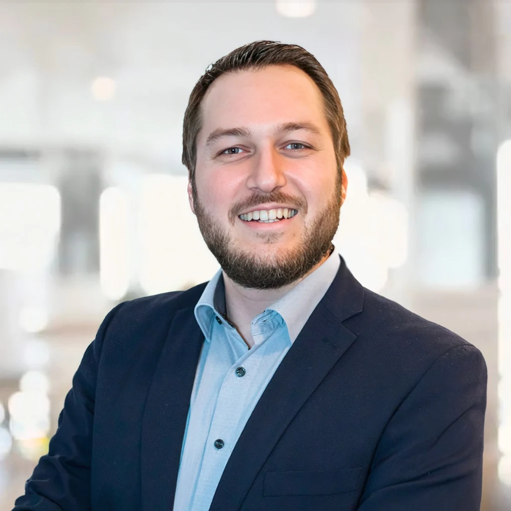 Ein lächelnder Mann in einem Anzug steht vor einem verschwommenen Hintergrund, der IT Sicherheit symbolisiert.